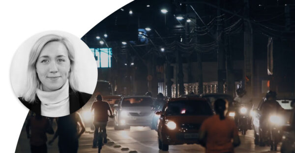 Cars and motorcycles driving on a street in the evening. People bicycle and walking on the side of the street. Profile image of Johanna Forseke.