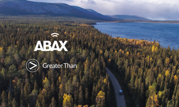 Car driving in the forest next to the ocean. In the horizon you can see the mountains. ABAX and Greater Than logos on top.