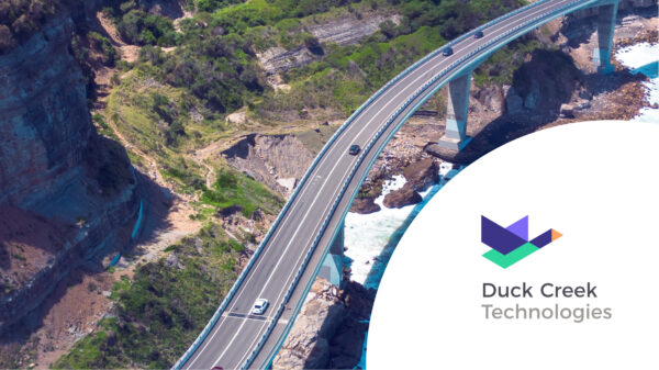 Bridge by the mountains and ocean, cars are driving. Duck Creek Technologies logo.