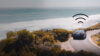 A black car driving by the beach with an icon above it showing it's connected