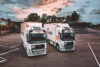 Two trucks branded with EB ROad Cargo logos parked at a parking lot with the sunset and trees in the background