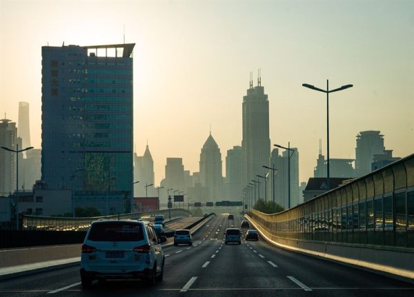 Sun is setting over buildings and cars are driving on the road