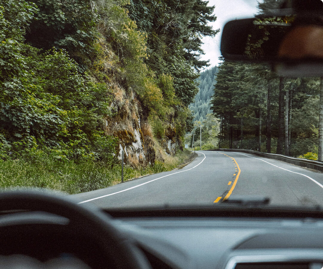 View from inside a vehicle driving on a scenic forest highway with curved road and tree-covered hills, representing safe and eco-friendly driving with Greater Than AI risk insights.