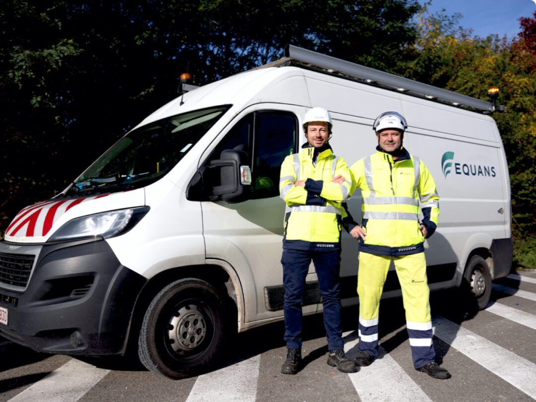 Two Equans field technicians in high-visibility workwear standing in front of a branded Equans service van, representing fleet safety and operational efficiency.