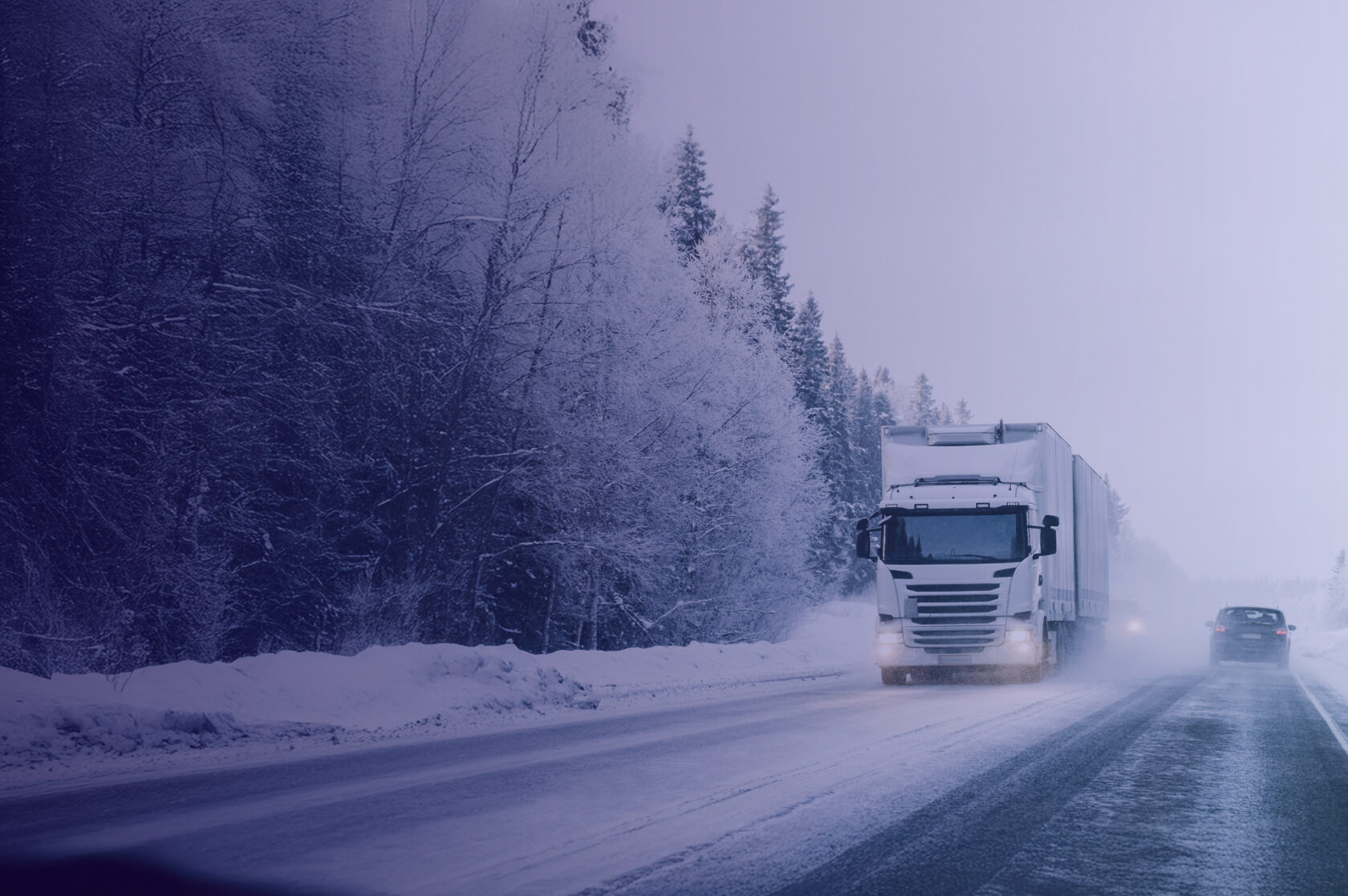 A white articulated truck driving on a winter road with snow and forest around. A passenger car is driving past it in the opposite direction.