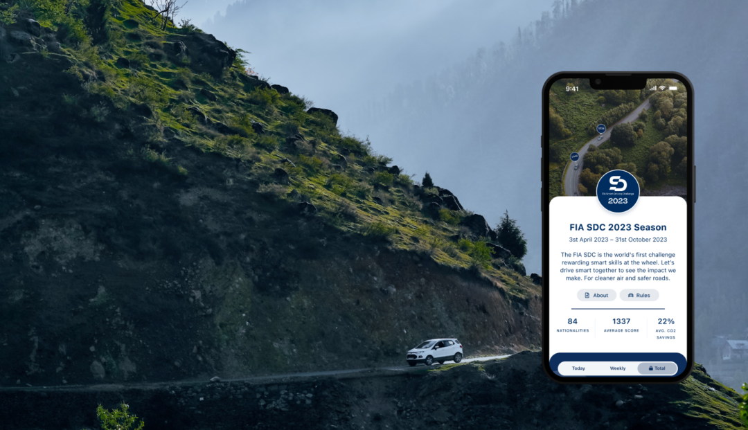 Car driving high up on a mountain. Phone showing FIA SDC app with 2023 season challenge.