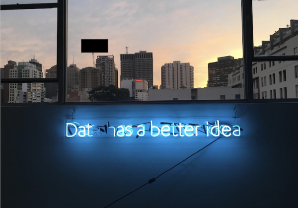 Neon sign saying Dat has a better idea and skyline showing in the background