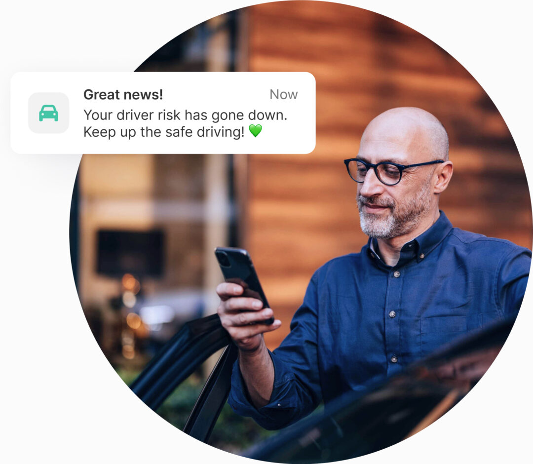 Man smiling while reading reduced driver risk notification on phone – safe driving rewards in telematics solution