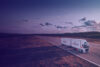 A truck branded with EB Road Cargo drives on a road in the sunset in an open landscape with forest around it