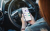 自動車保険のインセンティブプログラムにログインしているスマートフォンを持つ車内の女性