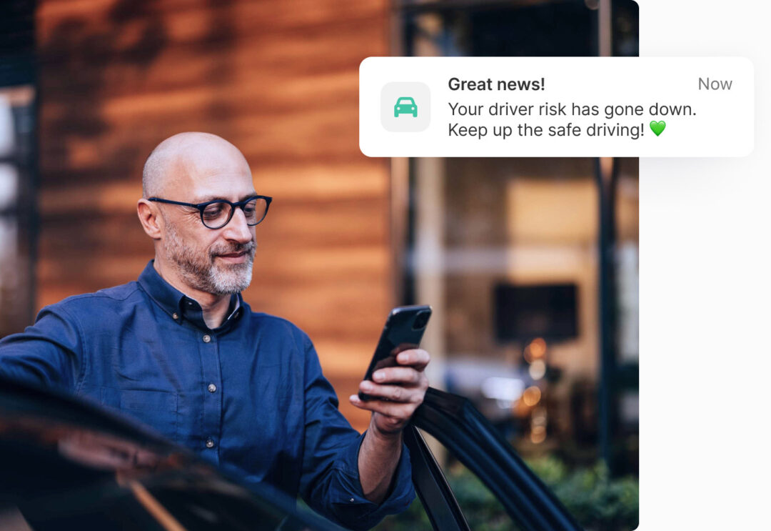 Man smiling while reading reduced driver risk notification on phone – safe driving rewards in telematics solution