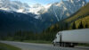 White truck driving on a road with snow-capped mountains in the background