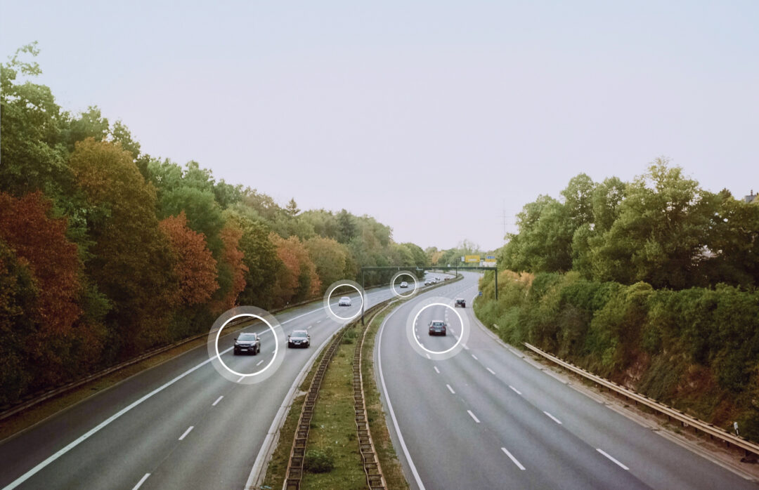 Cars driving on a highway with forest around it with circles highlighting several cars indicating that their driving data are being analyzed