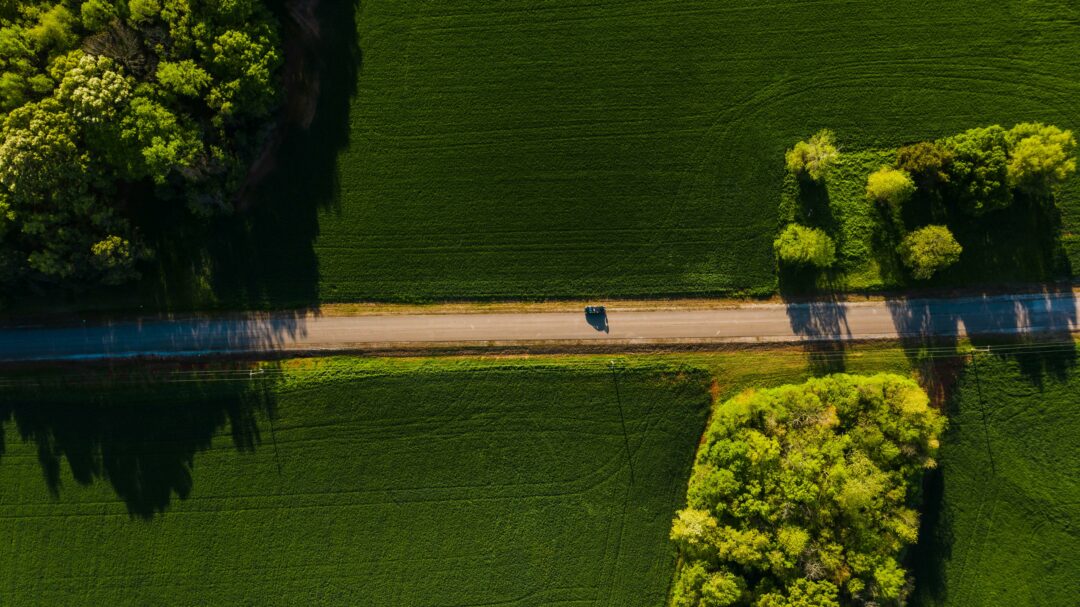 Car driving through a green landscape with fields and threes seen from above