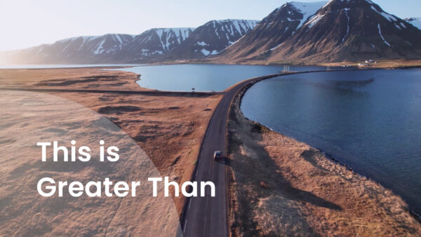 A car driving on a road with mountains and water around it. Text that says