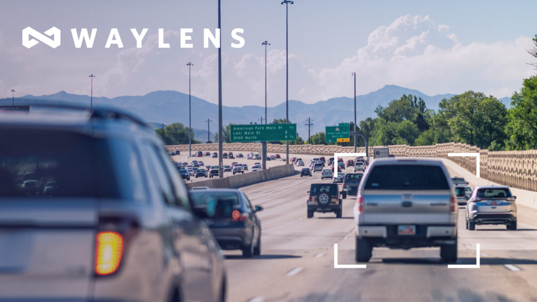 Busy highway scene with multiple vehicles driving toward green road signs indicating exits for American Fork Main Street and Lehi. A silver pickup truck is highlighted with a white focus frame, suggesting tracking or monitoring. The Waylens logo appears in the top left corner of the image.